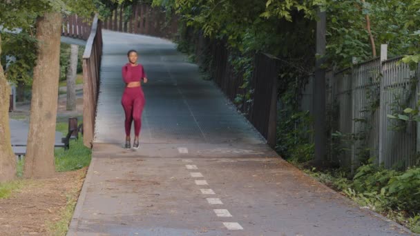 年轻美丽的非洲裔美国女孩穿着夏季运动服在公园里跑步，每天都在练习。健身女子在户外慢跑训练。体育活动和健康生活方式概念 — 图库视频影像