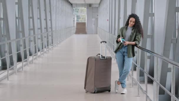 Joven dama caucásica mujer mujer pasajera turista viajero con maletas de pie en la terminal del aeropuerto sostiene tarjeta de embarque pasaporte billete de avión comprueba horario en el teléfono móvil va a bordo — Vídeo de stock