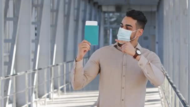 Retrato hispano hombre de negocios hombre viajero lleva máscara de protección médica sostiene en las manos pasaporte muestra billete de avión tren en el embarque viaje de negocios viaje de negocios vacaciones feliz con viajar — Vídeo de stock