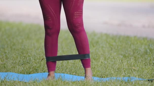 Piernas de cerca de pilates de chica negra más tamaño joven, entrenamiento de fitness práctica por banda de resistencia, haciendo ejercicios de entrenamiento con correa de goma. Activación muscular del glúteo entrenamiento al aire libre después de la cuarentena — Vídeo de stock