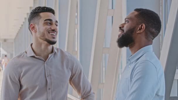 Dos colegas multirraciales hombres de negocios chico afroamericano y hombre hispano de pie en el pasillo en la oficina hablando conversación de comunicación apretón de manos informal abrazo masculino apoyo felicitación — Vídeos de Stock