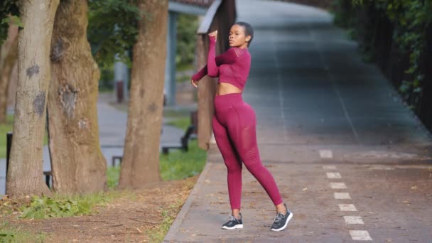 Niña africana practicando fitness, haciendo ejercicio al aire libre. Atleta femenina haciendo ejercicio de estiramiento sobre sus hombros y rodilla, calentando ejercicios antes de correr práctica concepto de estilo de vida saludable — Vídeos de Stock