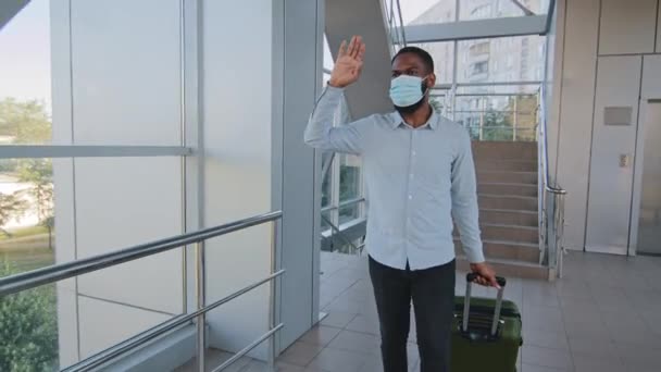 Hombre de negocios afroamericano inversor en máscara médica llega a un nuevo país en la terminal del aeropuerto se reúne con compañero gerente hispano codos saludos durante pandemia covid, viaje de negocios — Vídeo de stock