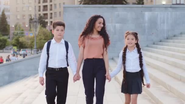 İspanyol aile kızı genç anne anne anne kız ve oğlu el ele tutuşuyor çocukları okula götürüyor öğrencileri ders için okula gidiyor açık havada yürüyüşe çıkıp gülümsüyor konuşuyorlar — Stok video