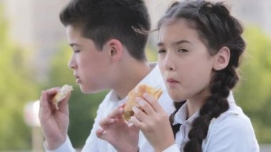 İki aç çocuk okul öğrencisi öğrenci erkek kardeş ve kız kardeş İspanyol çocuklar okul bahçesinde oturmuş çörek yiyorlar yemeklerin tadını çıkarıyorlar şişeden temiz su içiyorlar