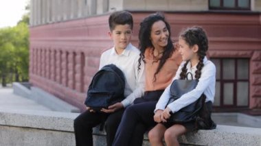 İspanyol aile kadını anne öğretmen, okul binasının arka bahçesinde iki küçük çocuk, öğrenciler, çocuklar, kız ve erkek çocuklar iletişim konuşmaları yapıyorlar.