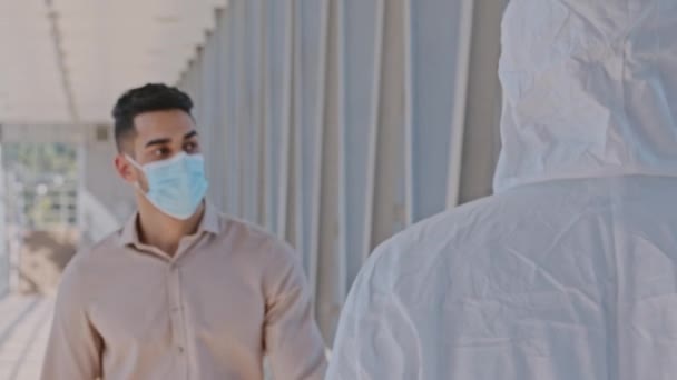 L'uomo ispanico indossa maschera facciale passeggiando per l'aeroporto al coperto nel centro commerciale lavoratore irriconoscibile in tuta protettiva medica ferma ragazzo misura la temperatura utilizzando termometro elettronico permette il passaggio — Video Stock