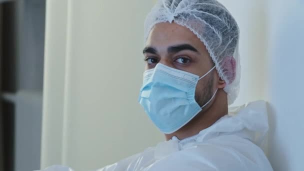 Portrait arabisch spanisch arzt mann chirurg medizinischer arbeiter trägt schutzkleidung uniform gesichtsmaske und mütze fühlt sich müde erschöpfung mund kampf covid coronavirus anschauen kamera wedeln kopf nein — Stockvideo