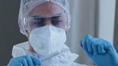 Genç doktor labaratuvar çalışanı Arap asıllı doktor koruyucu giysiler giyiyor steril üniforma şeffaf gözlük solunum cihazı ve kapak örnek alıyor covid corona virüsü için pamuk çubuğu kullanıyor.
