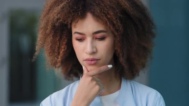 Kvinnligt porträtt utomhus afrikansk amerikansk ung pensiv flicka kvinna med lockigt hår djupt i tankarna tror planer minns funderar tänkande hyvling kommer med idé gör gest med pekfingret — Stockvideo