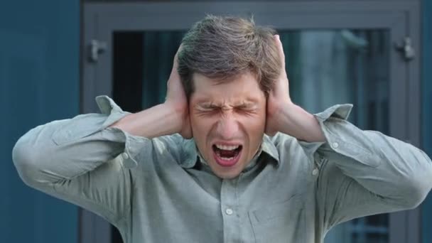 Too much noise. Anxious young professional shout NO cover ears with palms unable to hear loud music noisy sound. Angry frustrated businessman employer get mad hate listening disturbing noise outdoors — Stock Video