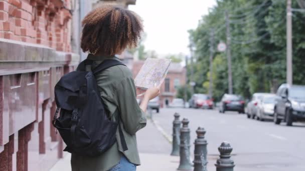 Młoda Afroamerykanka turystka z plecakiem podróżująca samotnie po wielkim mieście, trzymająca papierową mapę w rękach, sprawdzająca kierunek i trasę planowania. Zdolność nawigacji, samodzielna koncepcja podróży — Wideo stockowe