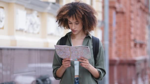 Atractiva joven afroamericana viajando y explorando hermosas vistas sosteniendo el mapa de la ciudad en las manos, disfrutando del tiempo de vacaciones. Bastante negro rizado turista chica examinar papel orientación — Vídeo de stock