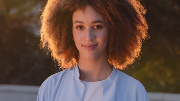 Vrouw buiten portret mooi jong verleidelijk etnisch afrikaans amerikaanse dame afro lachend meisje krullend model vrouw poseren op straat in zonlicht zonnestralen zonsondergang kijken naar camera glimlacht schattig vriendelijk — Stockvideo