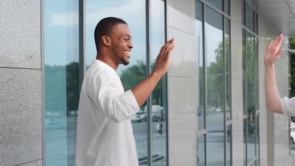 Afro americano homem preto africano cara atende data mulher caucasiana fazendo alta cinco gesto informalmente saudação andando ao ar livre cidade falando conversa masculino mostra tarde tempo diz sobre atraso — Vídeo de Stock