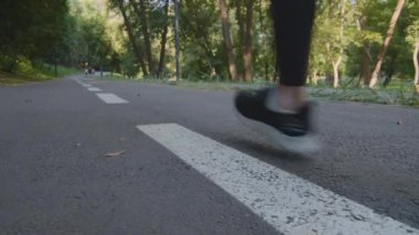 Parkta koşan kadın bacaklarının yakın çekimi. Tanınmayacak kadar zayıf, atletik kadın sporcu koşucu koşucu siyah tayt giyer ve şık spor ayakkabılar giyer sokak kardiyo antrenmanında koşar