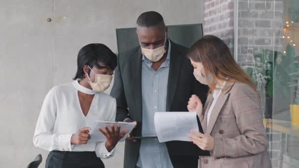 Tres compañeros de negocios de dibujos animados colegas en máscaras médicas gerente afroamericano chica y mujer caucásica mostrando documentos en papel para madurar afro jefe hombre discutiendo informe de información del contrato — Vídeos de Stock