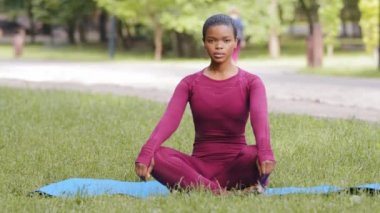 Paspas üzerinde oturan genç Afrikalı Amerikalı sporcu kadın yoga yaparken asana özfarkındalığı artırıyor, stres atağı kavramını geliştiriyor. Milenyum sakini siyah kadın yaz parkında çimenler üzerinde tek başına meditasyon yapıyor.