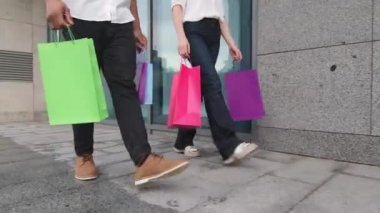 Erkek ve kadın bacakları beyaz kadın ve Afro-Amerikan erkek alıcılar alışveriş paketleri, indirimli tüketim konsepti taşıyorlar.