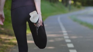 Koşu pistinde koşmaya hazırlanan kadın ayakları yakın plan. Sıska sporcu kadın koşucu siyah eşofmanlı koşucu esneme hareketleri bacak çekme kasları ısınma hareketleri açık hava koşusu hazırlıkları.