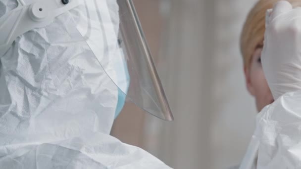 Γιατρός επιστήμονας ιατρός εργαζόμενος σε προστατευτική ομοιόμορφη διαφανές πρόσωπο ασπίδα γάντια λάτεξ χρησιμοποιεί βαμβάκι μάκτρο για να αναλύσει τα διαγνωστικά δείγμα σάλιου τεστ DNA σε καυκάσια μεσήλικη γυναίκα ανοίγει το στόμα — Αρχείο Βίντεο