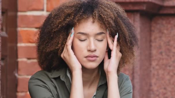 Face of unhappy young African American woman siting outdoors rubs temple, closed eyes suffers headache painful feelings chronic migraine hurt. Break up, difficult period of life concept closeup view — Stock Video