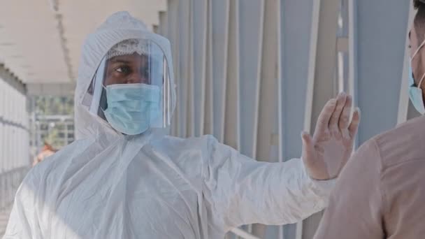 Afrikansk amerikansk manlig läkare i skyddande sterila kläder bär ansiktsskydd och medicinsk mask stoppar köpare inomhus mäter temperatur med trådlös termometer under covid pandemi — Stockvideo