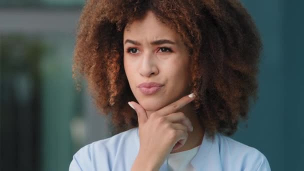 Femsle portrét venku afro americká tisíciletá zamyšlená dívka zmatený trapný kudrnatý žena model žena student stojící venku držení její bradu myšlení hluboko v myšlenkách plány rozhodování — Stock video