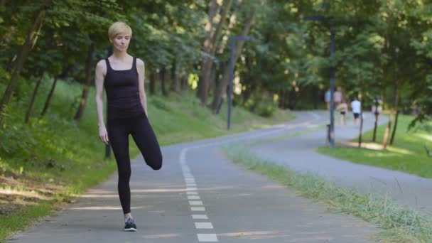 Středního věku běloška sportovkyně sportovkyně běžec běžec stojí městský park se připravuje na běhání běh venku protahuje nohy svaly protahování ohýbání kolena ráno cvičení sportovní cvičení — Stock video
