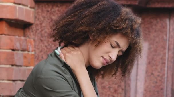 Closeup view Αφρο-Αμερικανίδα γυναίκα που κάθεται σε εξωτερικούς χώρους βιώνει έντονο πόνο στο λαιμό, τρίβοντας το για να ανακουφίσει την ένταση των μυών. Κοιλιακή οστεοχονδρωσία, κουρασμένη εργαζόμενη γυναίκα, καθιστική έννοια του τρόπου ζωής — Αρχείο Βίντεο