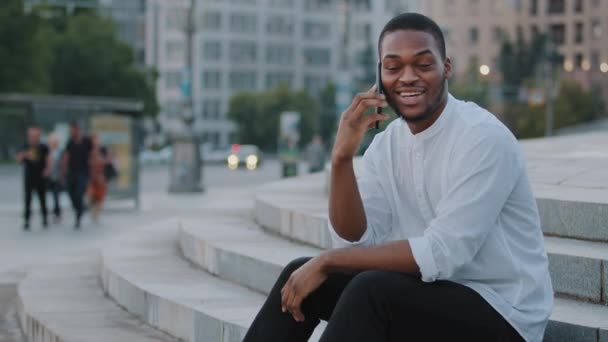 Hombre de negocios afroamericano estudiante africano chico negro étnico sentado en los escalones de la ciudad al aire libre hablando por teléfono contestando llamadas usando teléfono inteligente móvil para comunicar conversación charla distante — Vídeo de stock