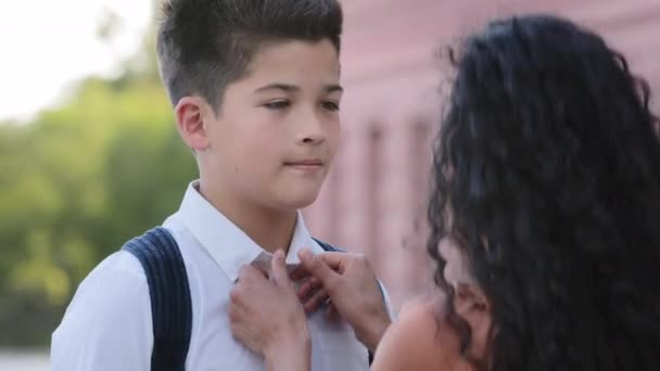 Irreconocible madre mujer morena mami cuello correcto en camisa de hijo acariciando niño en la cabeza hablando con colegial alumno cerca de la escuela clases abraza abrazos abrazos abrazos hispano niño abrazando mamá al aire libre — Vídeos de Stock