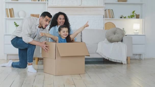 Spaanse familie huiseigenaren kopers ouders duwen kartonnen doos met dochter zitten in kind meisje wijzend naar voren met de vinger hebben plezier op het verplaatsen van de dag spelen verhuizing hypotheek — Stockvideo