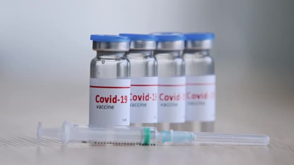 Frascos de cerca con medicamento de vacuna contra el virus covid19 remedio de coronavirus soporte de inmunización en la mesa de madera cerca de la jeringa manos femeninas en guantes de látex tomar una dosis de medicamento para la vacunación — Vídeo de stock