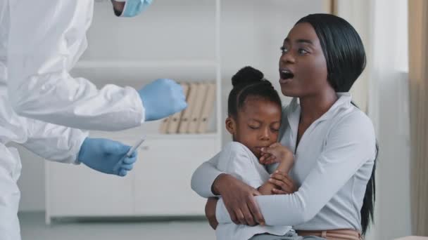 Enfermeira médica irreconhecível assistente médico em terno especial de proteção faz análise de teste PCR para covid19 coronavírus infecção mulher africana de mãe negra afro étnica abraçando criança filha assustada — Vídeo de Stock