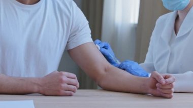 Tıbbi önlüklü, lateks eldivenli, kimliği belirsiz bir hemşire klinikte beyaz tişörtlü Arap hastaya kovid 19 virüsü Coronavirüs ilacına karşı aşı yapıyor.