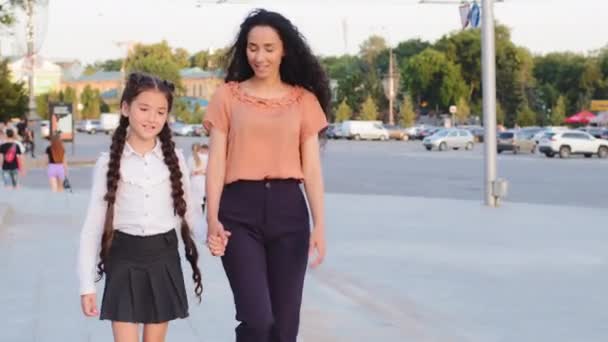 Famille hispanique jeune mère monoparentale tient la main de l'enfant fille écolière marcher dans la ville aller à l'école pour les classes parler souriant. Maman femme maman et petite fille enfant élève marche à l'extérieur — Video