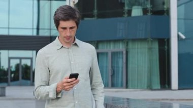 Mutlu Kafkas erkek yalnız başına yürüyen şehir caddesinde cep telefonu ile başvuru üzerine mesajlaşan, akıllı telefon kontrolü e-postası kullanan gülümseyen genç adam, internet ya da internet tarayıcısı