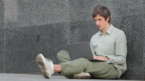 Smutný apatický depresivní mladý muž sedící venku s notebookem rozzlobený, rozzlobený, kvůli nedostatku baterií nebo bez internetu. Ten chlap dostal špatné zprávy, e-mail, stipendium zamítnuto, rezignace zpráva — Stock video