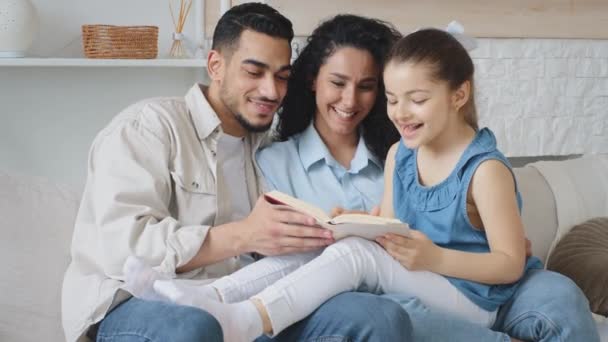 Hafta sonları evdeki kanepede oturup kitap okuyan İspanyol bir aile. Genç etnik ebeveynler, kız öğrencilere roman okumayı öğretiyor. Ders kitabı ev ödevi eğitimine yardımcı oluyor. — Stok video