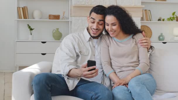 Hispanische glücklich lächelnde Ehepaar Familie kuschelt auf der Couch machen Videotelefonie Mann hält Smartphone sprechen Online-Chat-Konferenz mit Mobiltelefon drahtlose Gerät Fernkommunikation — Stockvideo