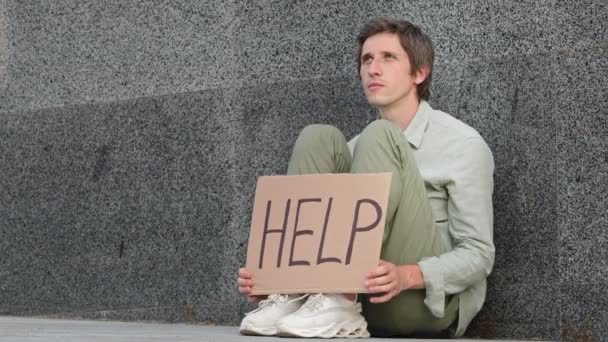 Triste joven desesperado sentado al aire libre con letrero, pancarta anunciando ayuda, víctima de desastre, cataclismo, crisis, pérdida de trabajo y dinero, dejado sin hogar. Problemas masculinos, concepto de asistencia mutua social — Vídeos de Stock