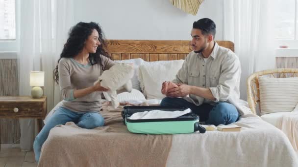 Spanjorska nygifta par makar man och hustru pojkvän och flickvän leende kvinna och koncentrerad man sitter på sängen sätta saker i resväskan för att resa utomlands smekmånad semester — Stockvideo