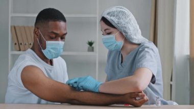 Kafkasyalı kadın doktor hemşire özel üniformalı tıbbi maske takıyor. Kovid 19 aşısı koronavirüs antibiyotik ilacından hastanedeki Afro Amerikalı zenci erkek hastaya aşı yapıyor.