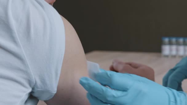 贴身医生护士用乳胶手套擦拭男人的黑皮肤用棉毛和酒精将注射器和针头注射到非洲男人的肩上，接种治疗概念 — 图库视频影像