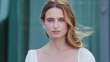 Geniş beyaz tişörtlü, kameraya bakan genç bir kadının portresi. Güzel bir bayan, dişçi kliniğinde dişlerini beyazlatıyor. Modern bina arka planında poz veriyor.