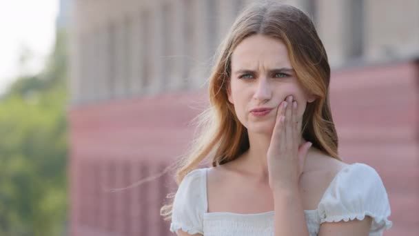 Mujer de cerca parada al aire libre tocando la mejilla, sufriendo de dolor, sintiendo dolor de muelas. Chica adulta joven tiene problemas dentales, necesita tratamiento médico. Caries dental, caries bucal problema — Vídeos de Stock