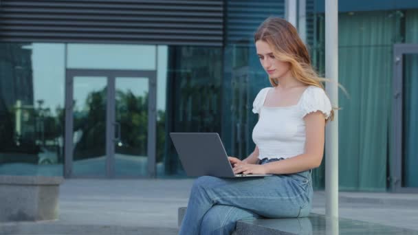 Atrakcyjna dziennikarka pracująca online z laptopem, siedząca na zewnątrz patrząca na ekran, pisząca na maszynie, poważna młoda kobieta pisząca blog lub rozmawiająca ze znajomymi w sieci społecznościowej — Wideo stockowe