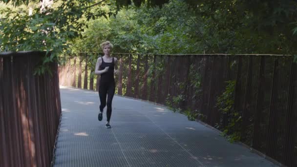 Smal atletisk stark aktiv kvinna sportskvinna löpare joggare i sportkläder energiskt snabb kör jogging maraton morgon kör i park bridge cardio motion fitness träning träning — Stockvideo