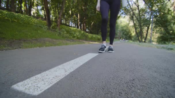 Fermez les jambes féminines. Athlétique femme mince athlète en noir vêtements de sport promenades dans le parc en plein air avant le jogging met bouteille d'eau sur la piste liens dentelle sur chaussures de baskets pour se préparer à l'entraînement marathon — Video